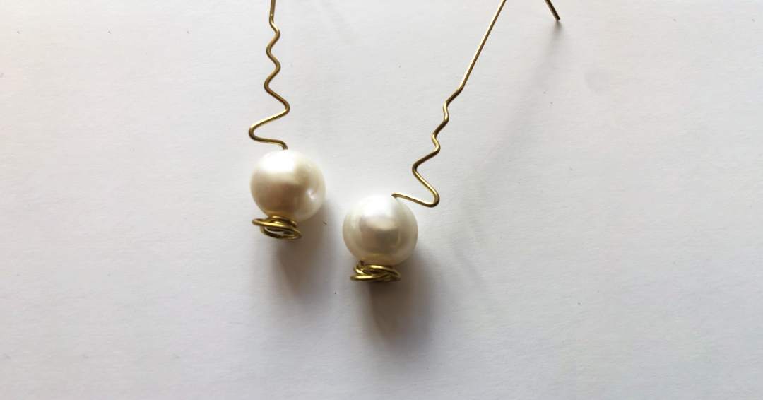 Pendientes largos en color dorado con una perla al final de cada uno. Elaborados artesanalmente con bronce de media caña.
